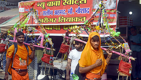 Kanwariyas walk past a shop on which banners with shopkeeper's name was put up on Kanwar Marg after an order issued by Uttar Pradesh Government, in Muzaffarnagar, Saturday, July 20, 2024.
