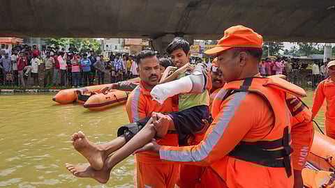 NDRF personnel carry a boy with a plaster cast on his arm as they conduct rescue operations after floodwater entered the Kendriya Vihar apartment following heavy rain, in Bengaluru.