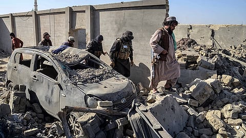 Taliban security personnel walk past a damaged car in the Spin Boldak district of Kandahar province.