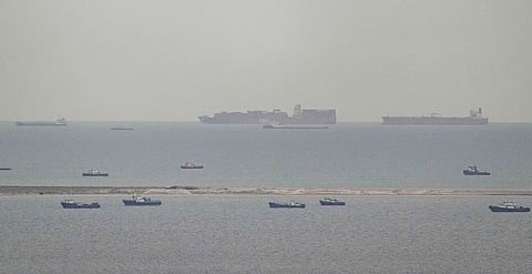 Fishing boats dot the sea as cargo ships, in the background, sail through the Arabian Gulf toward the Strait of Hormuz off the United Arab Emirates