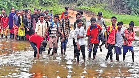 ಹೆಗಲಲ್ಲಿ ಬ್ಯಾಗ್ ಏರಿಸಿಕೊಂಡು ಹೊಳೆ ದಾಟಿಕೊಂಡು ಹೋಗುತ್ತಿರುವ ಮಕ್ಕಳು