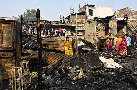 A woman stands amid charred remains after a fire broke out spreading to around 500 shanties near Rithala metro station, at Rohini area, in New Delhi, early Saturday