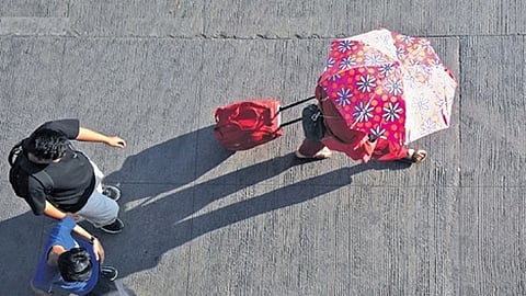 A passenger at Bengaluru’s Kempegowda Bus Terminal uses an umbrella to protect herself from the summer heat on Thursday