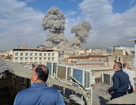 People watch as smoke rises on the skyline after an explosion in Tehran.