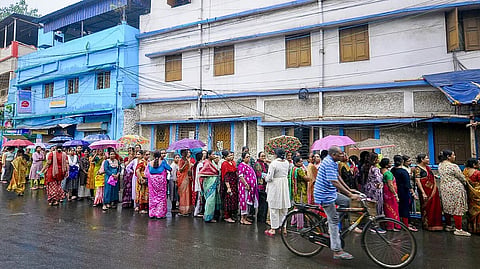People wait in queues amid rain before casting their votes