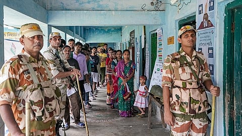Security personnel stand guard as voters wait in a queue to cast their votes at a polling station during a repoll ordered by the Election Commission