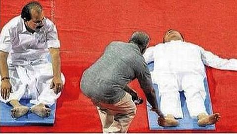 ಯೋಗ ಮಾಡುತ್ತಿದ್ದಾಗ ಗಾಢನಿದ್ದೆಗೆ ಜಾರಿರುವ ಸುರೇಶ್ ಪ್ರಭು ಅವರನ್ನು ತರಬೇತುದಾರರು ಎಬ್ಬಿಸುತ್ತಿರುವ ಚಿತ್ರ